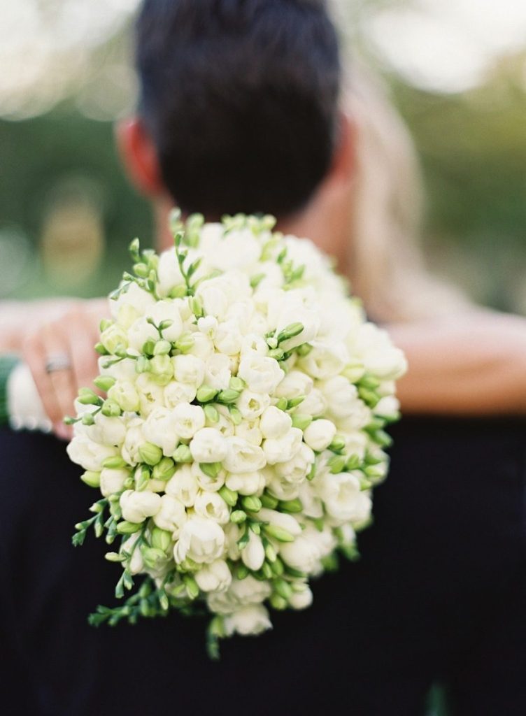 In questa foto un bouquet di fresie poggiate sulla schiena di uno sposo ripreso di spalle abbracciato dalla sposa