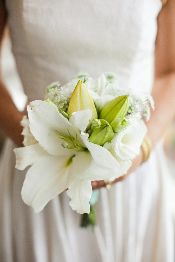 In questa foto le mani di una sposa che tiene tra le mani un bouquet di gigli bianchi