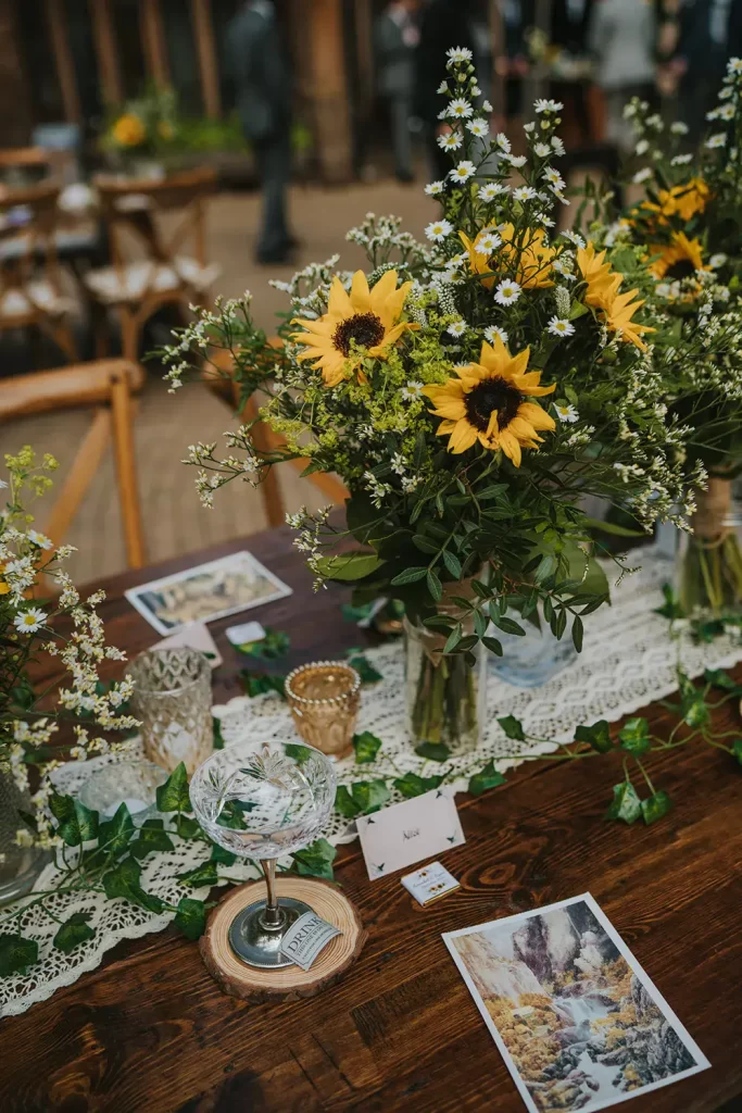 In questa foto il dettaglio di un tavolo per matrimonio in legno nudo decorato con un runner di pizzo su cui sono disposti vasetti con girasoli e nebbiolina