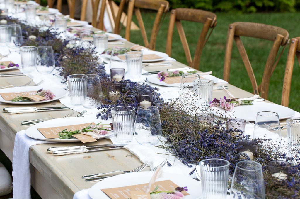 In questa foto il dettaglio di un tavolo di nozze allestito su un prato e decorato con un runner di lavanda 