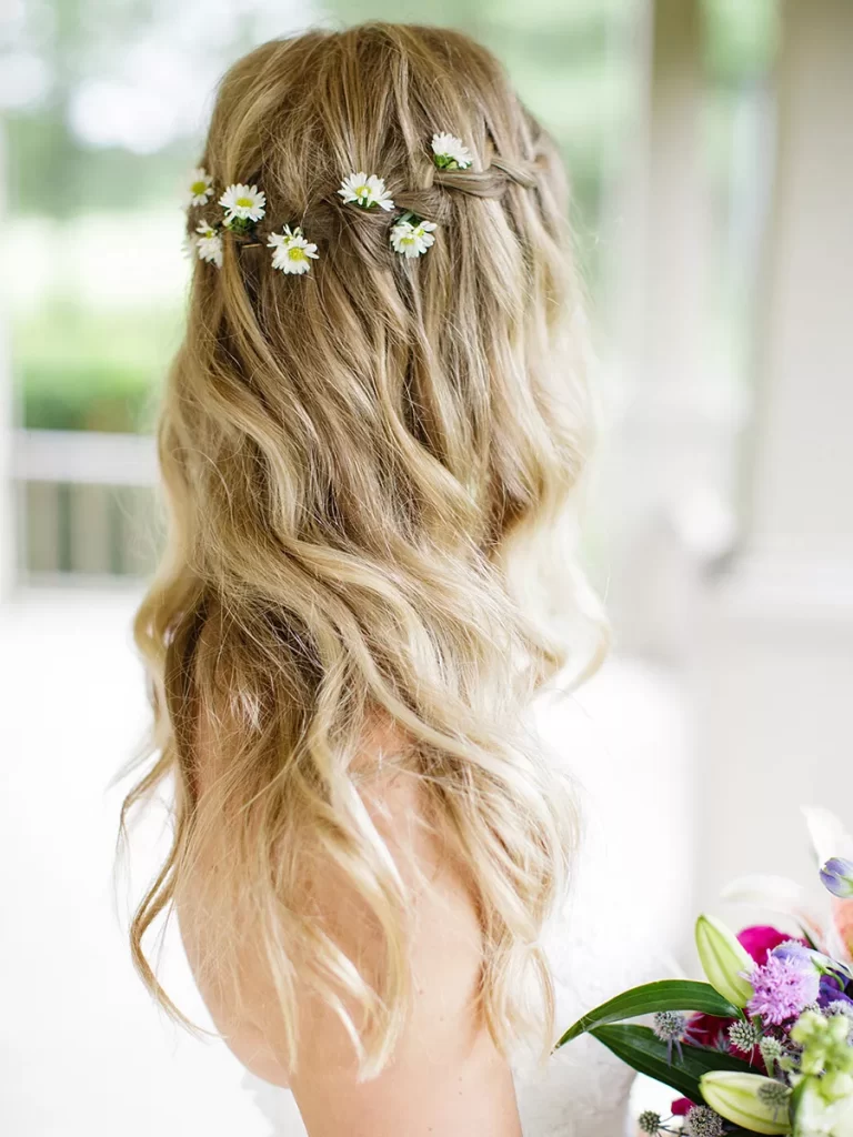 In questa foto una sposa ripresa di spalle con capelli mossi e sciolti e una  piccola corona di margherite