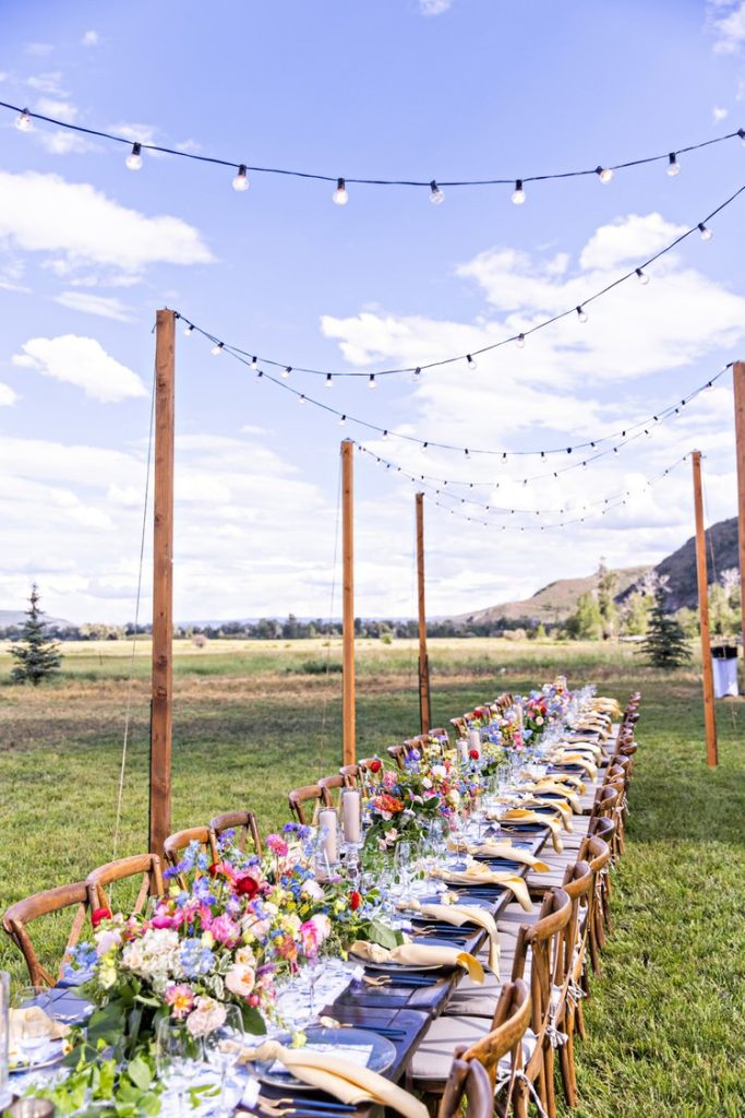 In questa foto un tavolo imperiale su un prato per un matrimonio in stile country chic con fiori di campo colorati, piatti blu e tovaglioli gialli