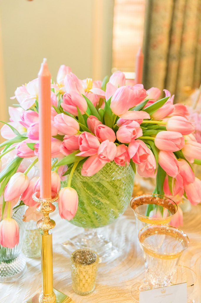 In questa foto un centrotavola di un tavolo per matrimonio composto da un vaso di cristallo con tulipani rosa. Sul tavolo sono disposti anche portacandele colore oro con candele rosa e bicchiere di cristalli con bordatura colore oro