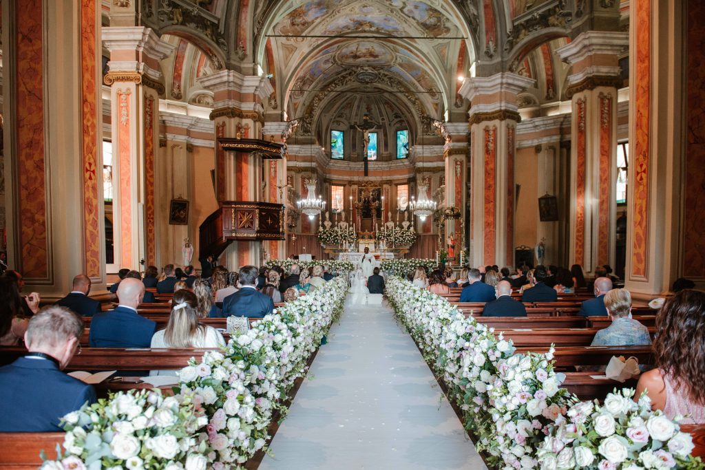 In questa foto una chiesa per matrimonio con la navata centrale decorata con un tappeto bianco, rose bianche e colore rosa