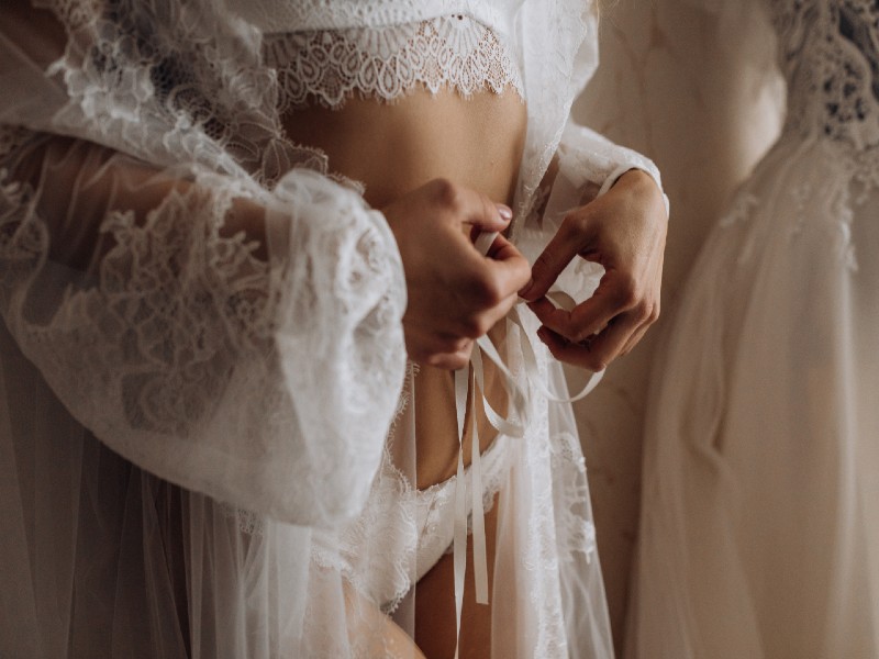 In questa foto il dettaglio una ragazza indossa il suo intimo da sposa legando il nastro della sua vestaglia in pizzo