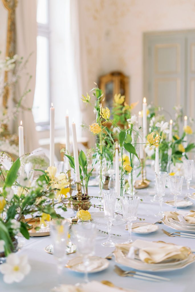 In questa foto il dettaglio di una decorazione di fiori matrimonio gialli su un tavolo imperiale con tovagliato azzurro, portacandele colore oro e candele, piatti e tovaglioli bianchi