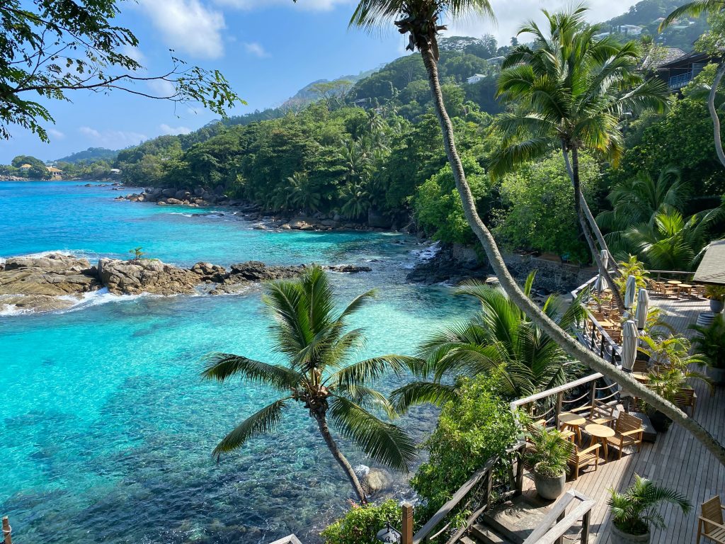 In questa foto la costa di un'isola delle Seychelles vista dall'alto con palme, scogli e un porticato