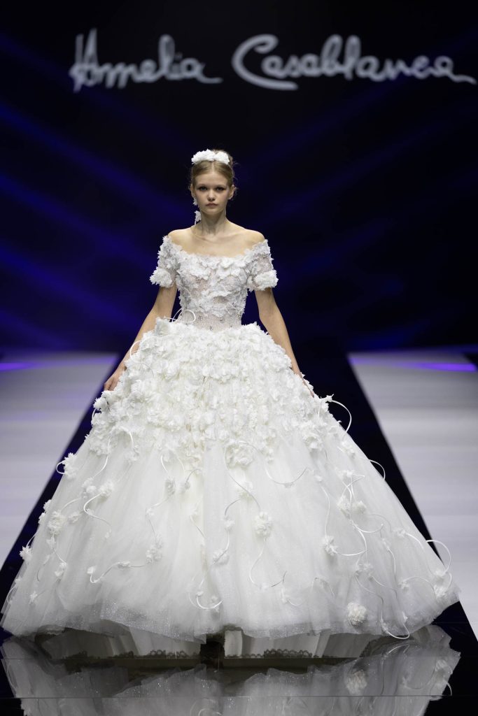 In questa foto la modella indossa un abito da sposa Amelia Casablanca 2023 con gonna ampia e fiori 3D.