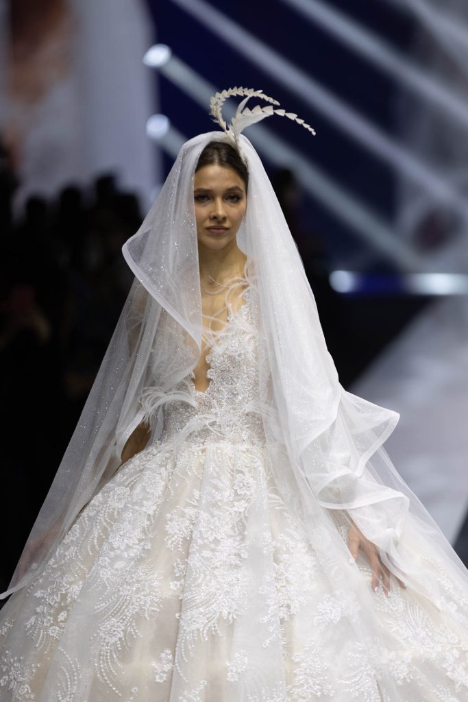 In questa foto la modella indossa un abito da sposa Amelia Casablanca 2023 con ricami e piume.