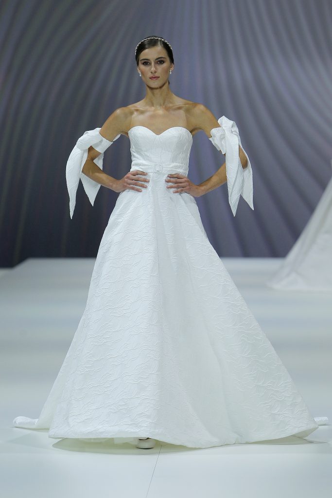 In questa foto una modella indossa un abito da sposa Nicole Milano 2023, visto sulla passerella della BBFW 2022