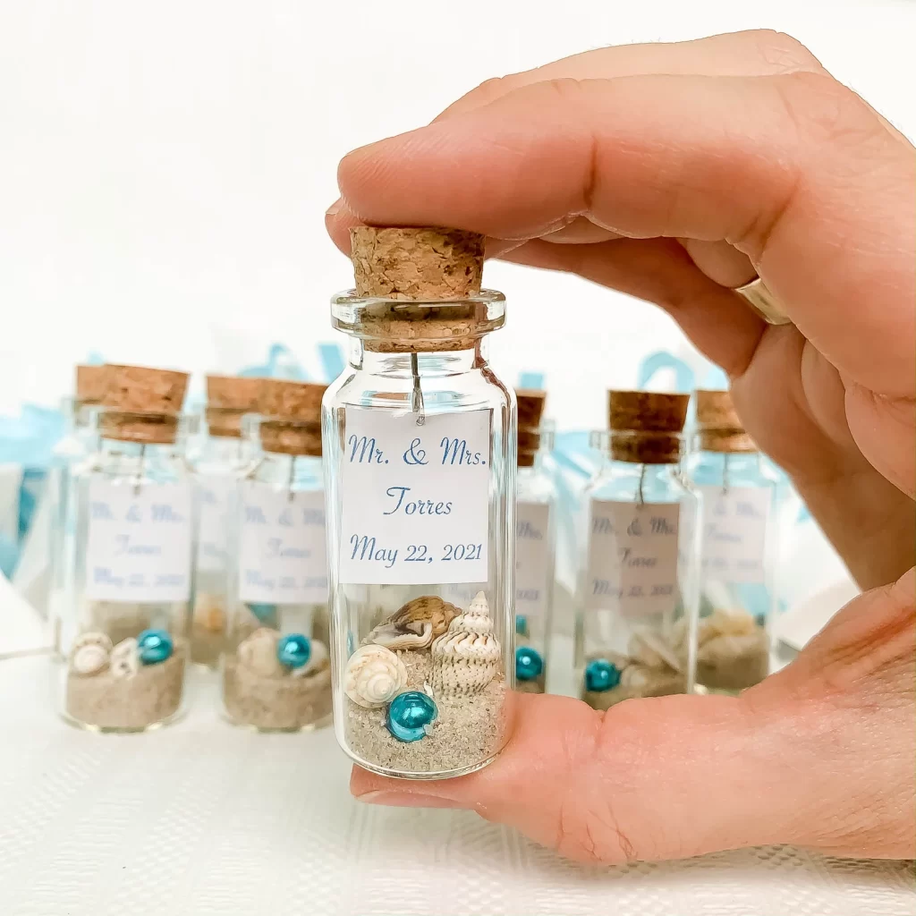 In questa foto bomboniere per matrimonio a tema mare a forma di piccola bottiglietta di vetro con tappo in sughero con sabbia e piccole conchiglie