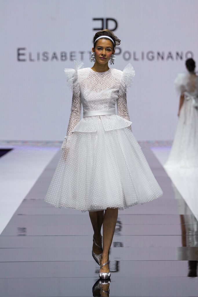 La modella indossa un abito con gonna al ginocchio della nuova collezione sposa Elisabetta Polignano 2023.