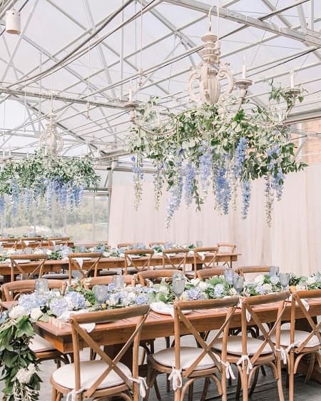 In questa foto, composizioni pensili e lunghi centrotavola floreali dai toni delicati dell' azzurro polvere e glicine sono i fiori per matrimonio stile Shabby