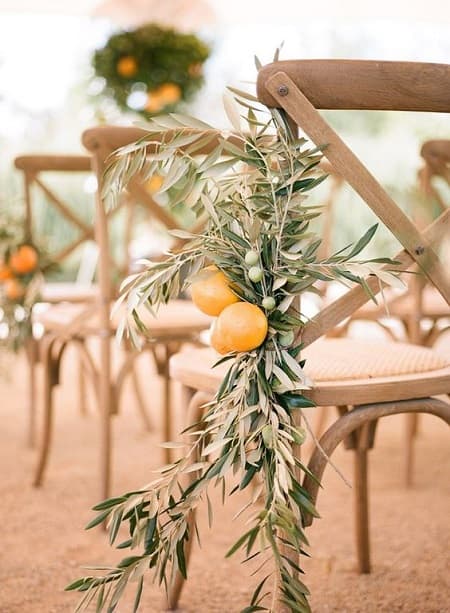 In questa foto, una decorazione floreale realizzata con limoni e rami d'ulivo decora le sedie per gli invitati di un matrimonio stile siciliano all'aperto