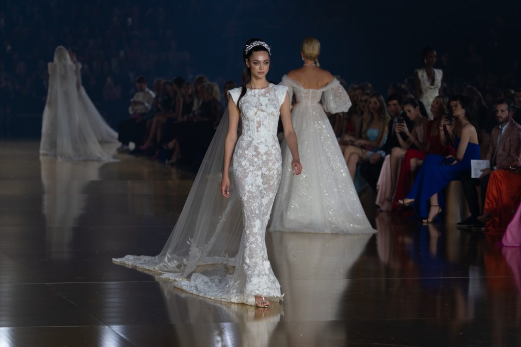 In questa foto la modella indossa un abito da sposa Atelier Pronovias 2023 con pizzo. 