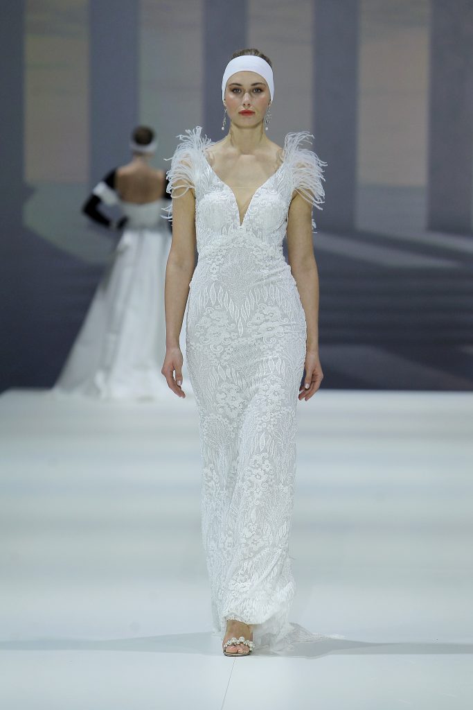 In questa foto la modella indossa un abito da sposa Higar Novias 2023 con pizzo e piume.