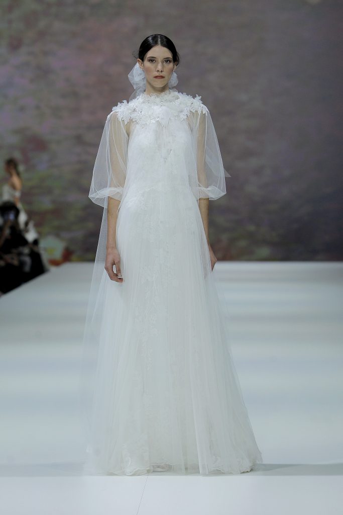 In questa immagine la modella indossa un abito da sposa Marchesa for Pronovias 2023 con ricami. con maniche di tulle.