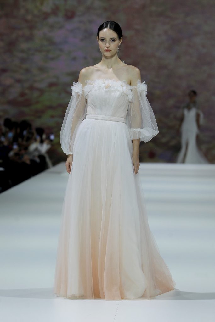 In questa immagine la modella indossa un abito da sposa Marchesa for Pronovias 2023 con sfumature color pesca.