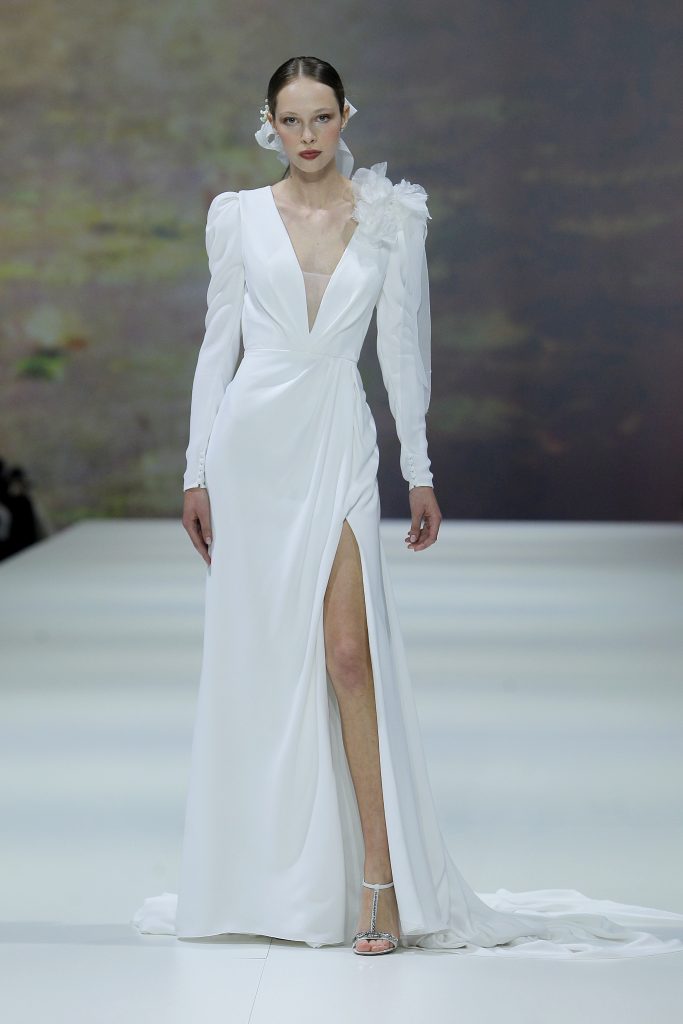 In questa immagine la modella indossa un abito da sposa della collezione di abiti da sposa Marchesa for Pronovias 2023 con profondo scollo a V.