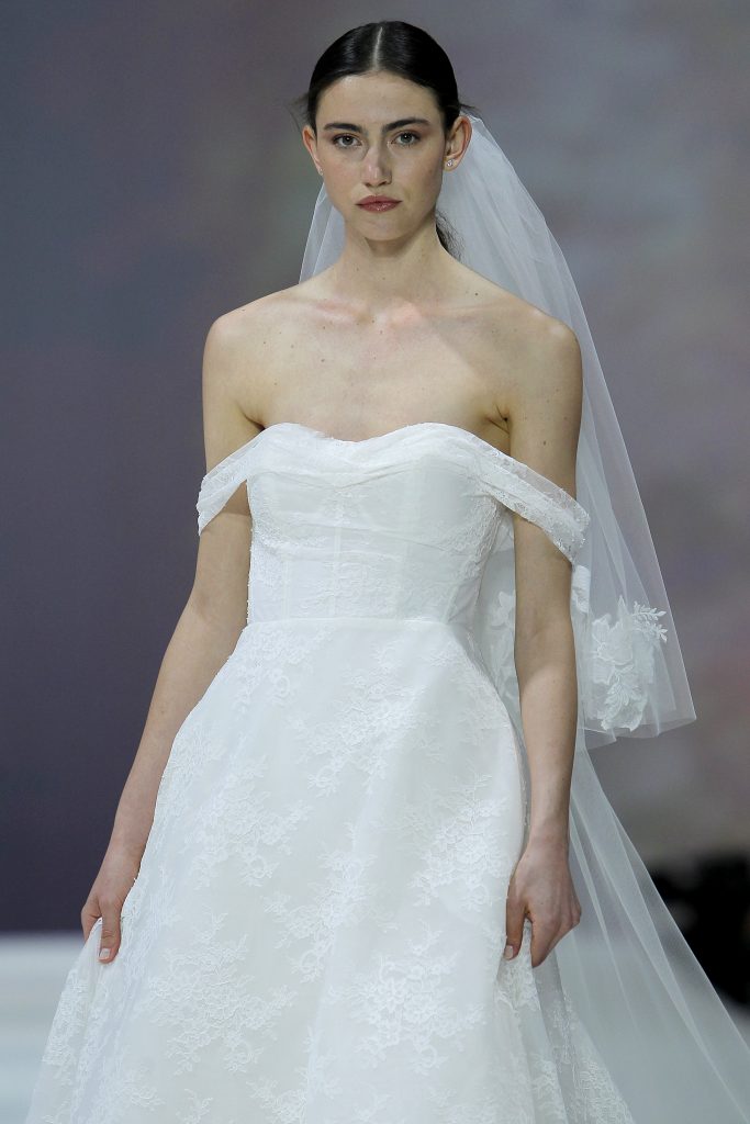 In questa immagine la modella indossa un abito da sposa Marchesa for Pronovias 2023 di pizzo.