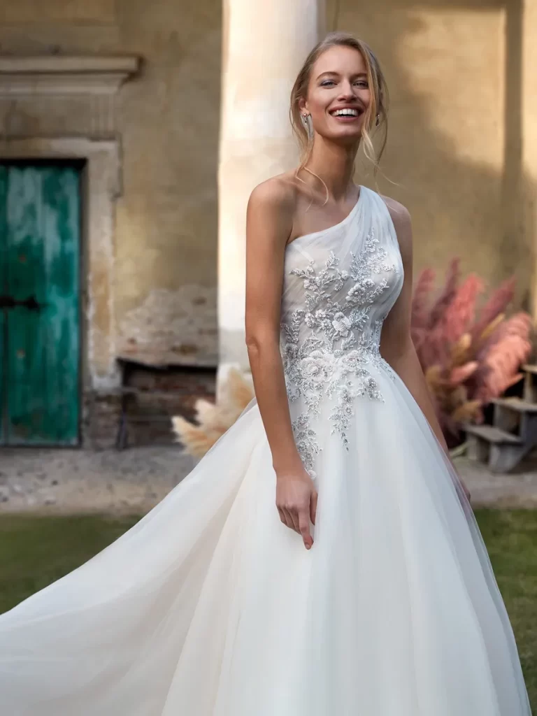 In questa foto una modella indossa un abito da sposa monospalla 2022 della collezione Nicole Milano.