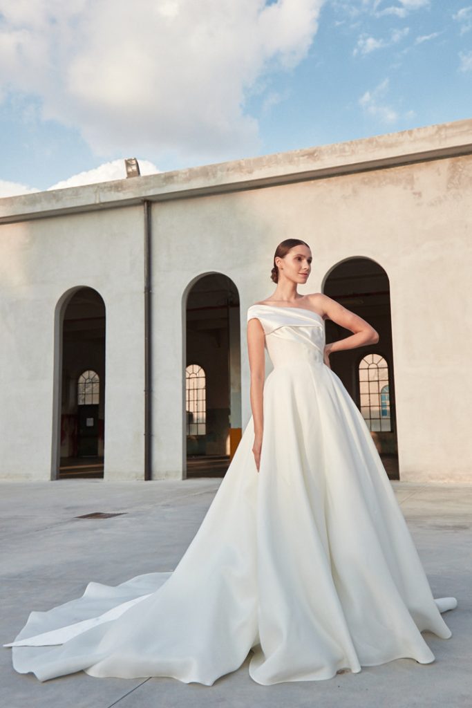 In questa foto una modella indossa un abito da sposa monospalla 2022 della collezione Peter Lagner
