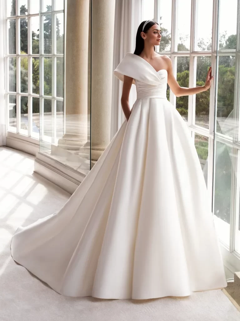 In questa foto una modella indossa un abito da sposa monospalla 2022 della collezione Pronovias.