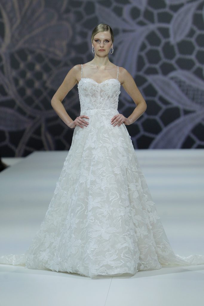 In questa foto la modella indossa un abito da sposa Nicole Milano 2023  con decori floreali.