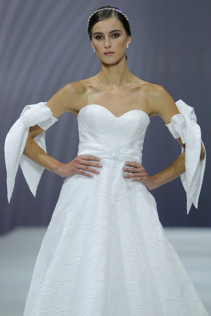 In questa foto la modella indossa un abito da sposa Nicole Milano 2023 con fiocchi sulle maniche.