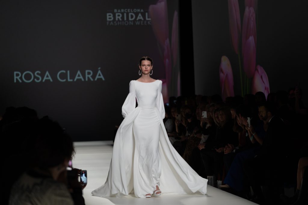 In questa foto la modella indossa un abito da sposa Rosa Clarà 2023 a sirena con maniche lunghe.