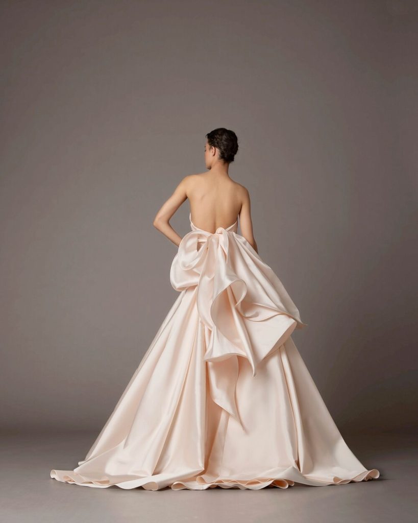 In questa foto una modella indossa un abito da sposa schiena scollata 2022 della collezione Antonio Riva con scollo e maxi fiocco.