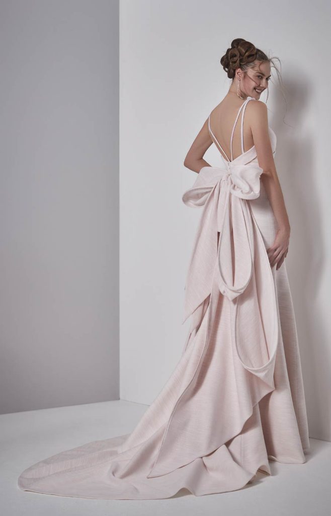 In questa foto una modella indossa un abito da sposa schiena scollata 2022 della collezione Elisabetta Polignano con scollo profondo e maxi fiocco.