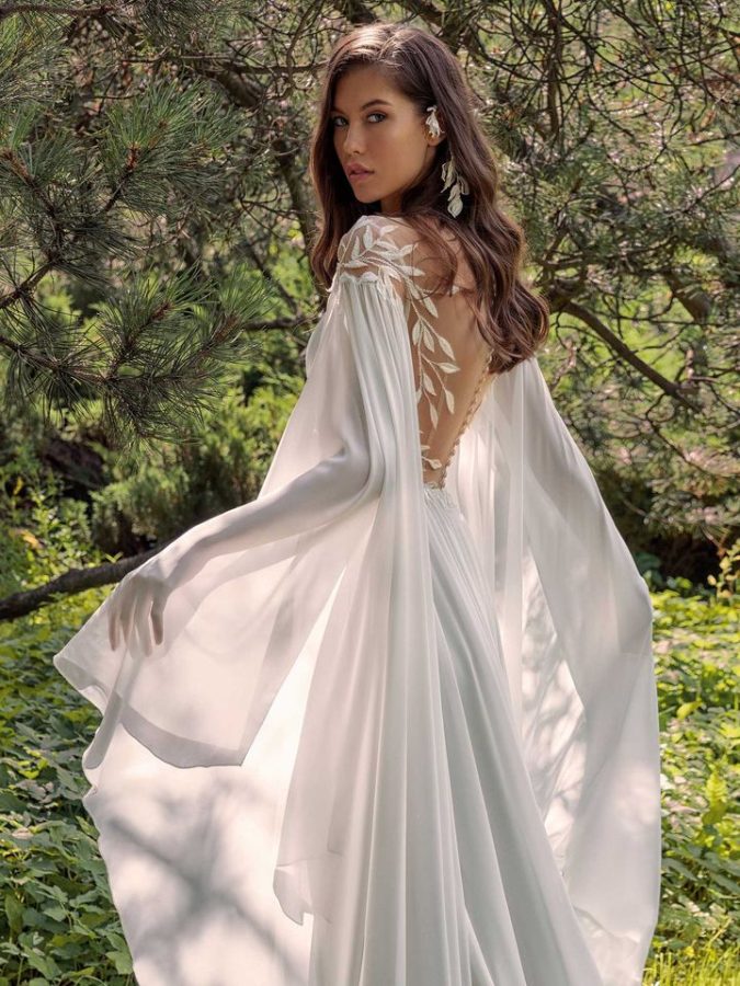 In questa foto una modella indossa un abito da sposa schiena scollata 2022 della collezione Papilio con scollo profondo e maniche lunghe.