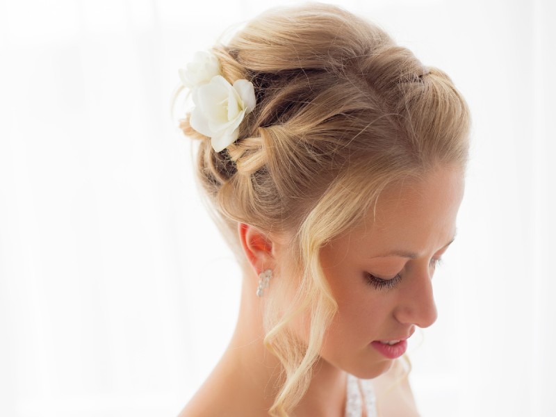 In questa foto una ragazza bionda ripresa dall'alto mentre mostra la sua acconciatura da sposa con capelli raccolti decorata con fiori bianchi freschi