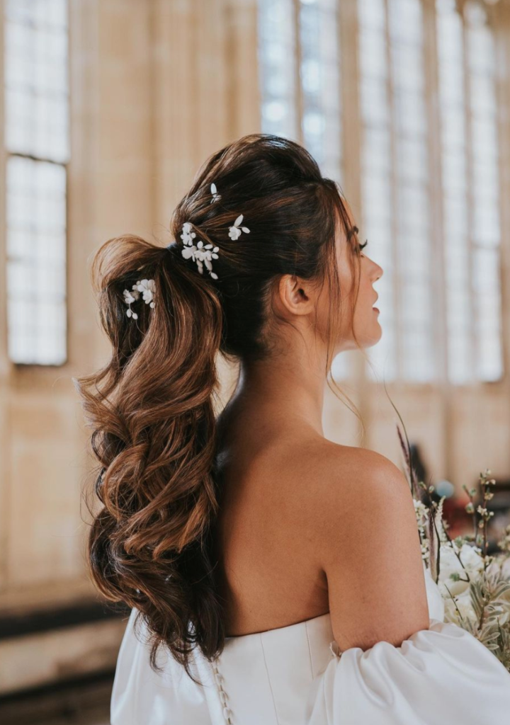 In questa foto una sposa di profilo con una coda alta con onde morbide e decorata con fermagli di perline