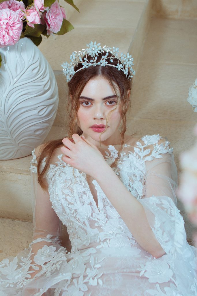 In questa foto una modella indossa un a corona con pietre dure colore turchese che creando un intreccio di di fiori. Indossa un abito da sposa con fiori 3D