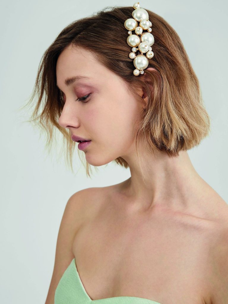 In questa foto una modella di profilo indossa sui capelli corti un fermaglio con perle di diverse dimensioni