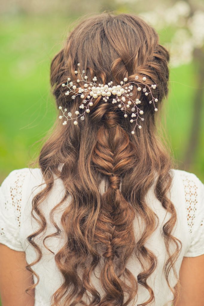 In questa foto una sposa di spalle con un'acconciatura semiraccolta con trecce decorata con un ramage di perline