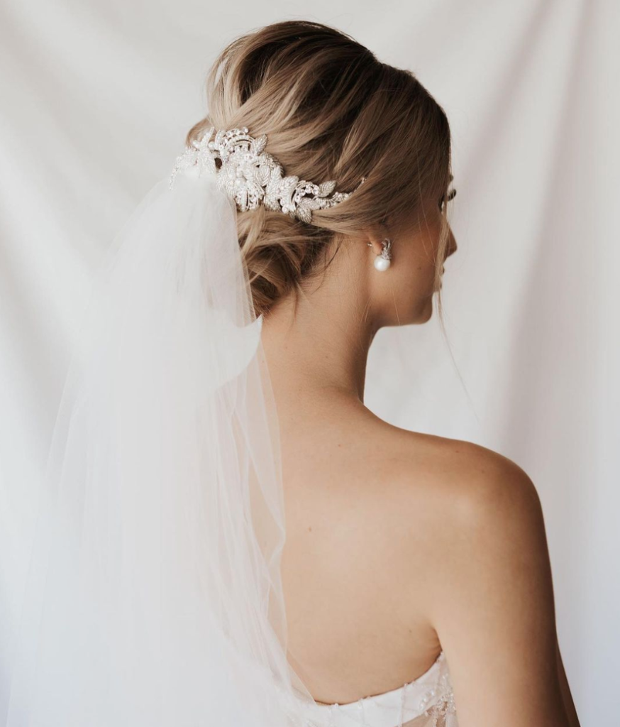 In questa foto un'acconciatura da sposa con velo e chignon decorato con fermaglio di fiori e cristalli