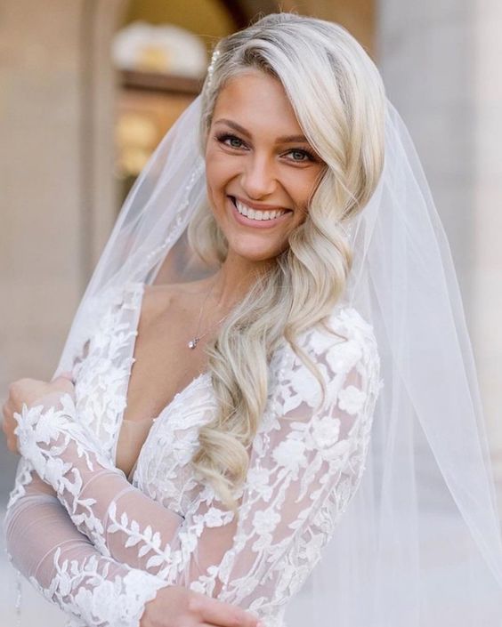 In questa foto una sposa sorridente con acconciatura laterale con capelli mossi e velo