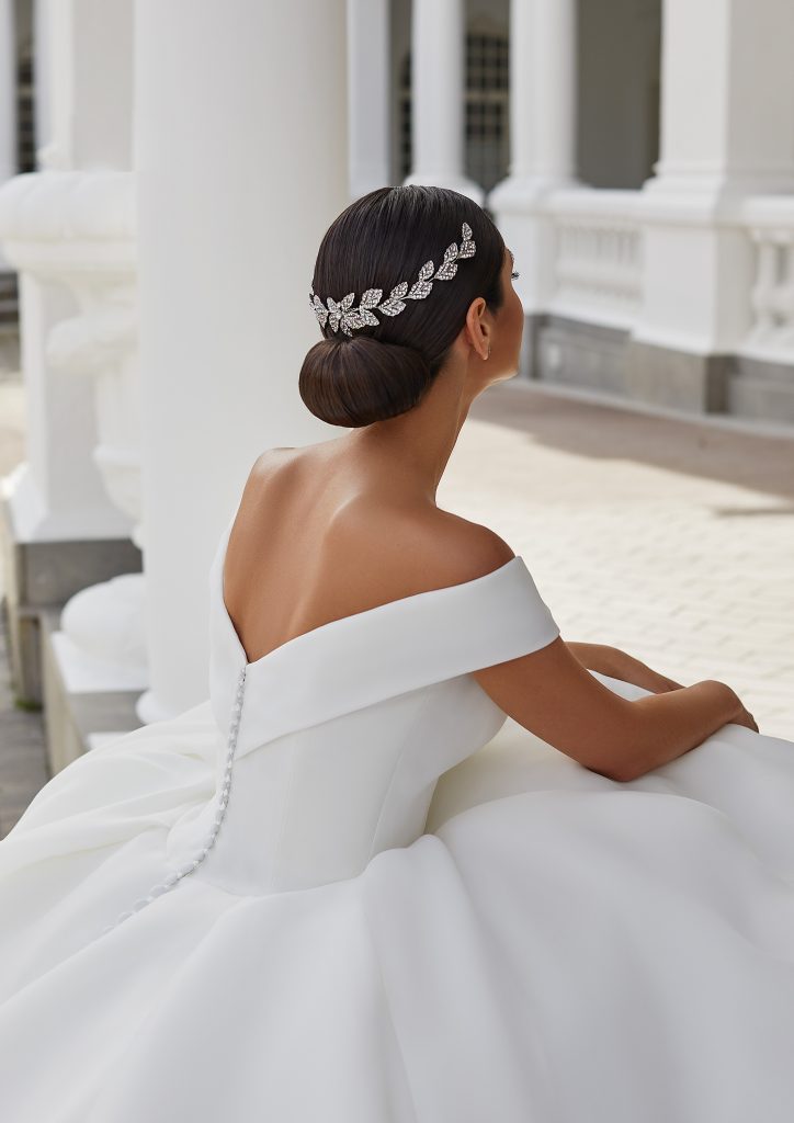 In questa foto una modella di spalle con uno chignon basso e un fermaglio prezioso a forma di mezza corona sulla nuca 