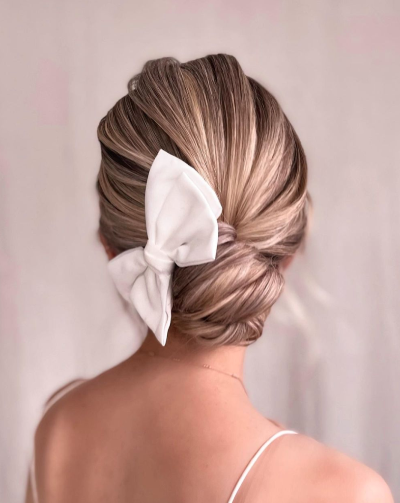 In questa foto una sposa con uno chignon basso fermato da un grande fiocco di colore bianco