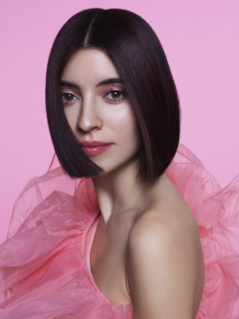 In questa foto una modella con un'acconciatura da sposa con capelli corti e lisci. Indossa un abito rosa di tulle