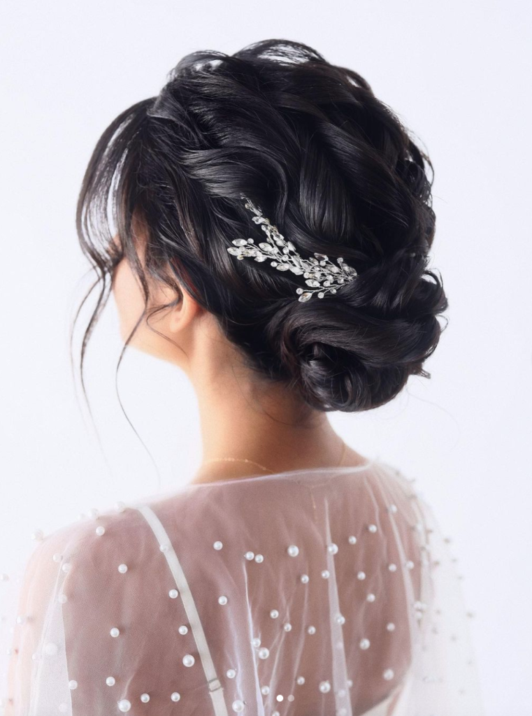 In questa foto una sposa di spalle con un raccolto morbido sul collo, capelli mossi e un fermaglio con perline colore argento