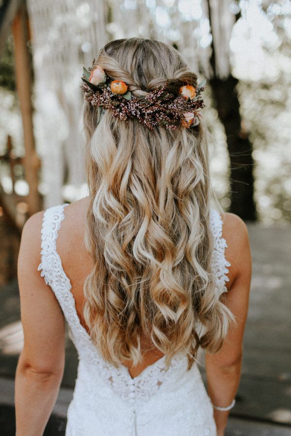 In questa foto una sposa di spalle con capelli mossi semiraccolti in una treccia con fiori colore arancone e viola