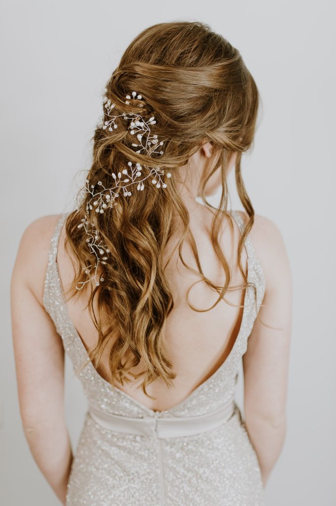 In questa foto una sposa di spalle con un'acconciatura semiraccolta con capelli mossi decorati con un ramage di perline