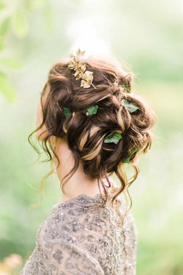 In questa foto un'acconciatura da sposa con capelli raccolti e mossi decorata con foglioline e un fermaglio di colore oro