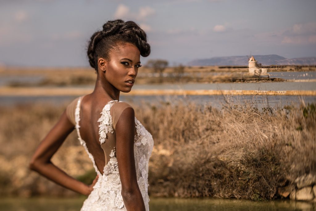 In questa foto una modella posa nelle saline di Marsala con un'acconciatura da sposa raccolta trasformabile. Indossa un abito di pizzo con schiena scoperta 