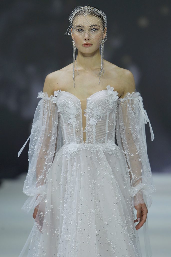 In questa foto la modella indossa un abito da sposa romantico 2023 con bustier trasparente con fiori e maniche removibili