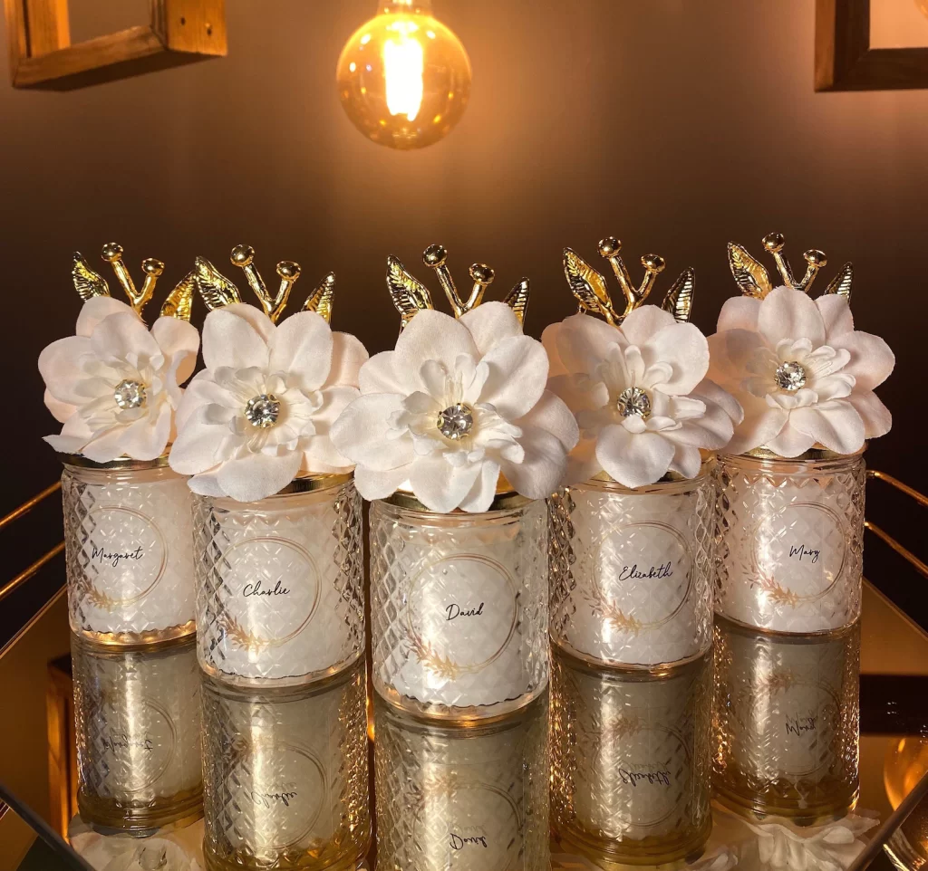 In questa foto bomboniere per matrimonio eleganti in cristallo e bordi colore oro con candele bianche e decorazione a forma di fiore colore bianco e oro